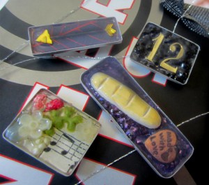 Guess these consist of an arrow, District 12, Peeta's bread, and Rue's flowers and lullaby. And each seems to come in its own tin.